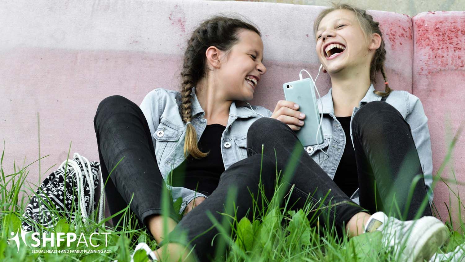 Two young girts sitting on the grass laughing together.