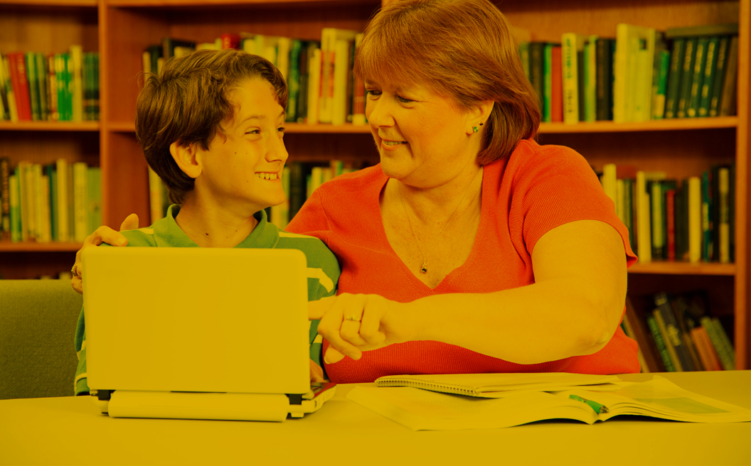 Young boy with a intellectual disability sitting with a teacher in front of a laptop.