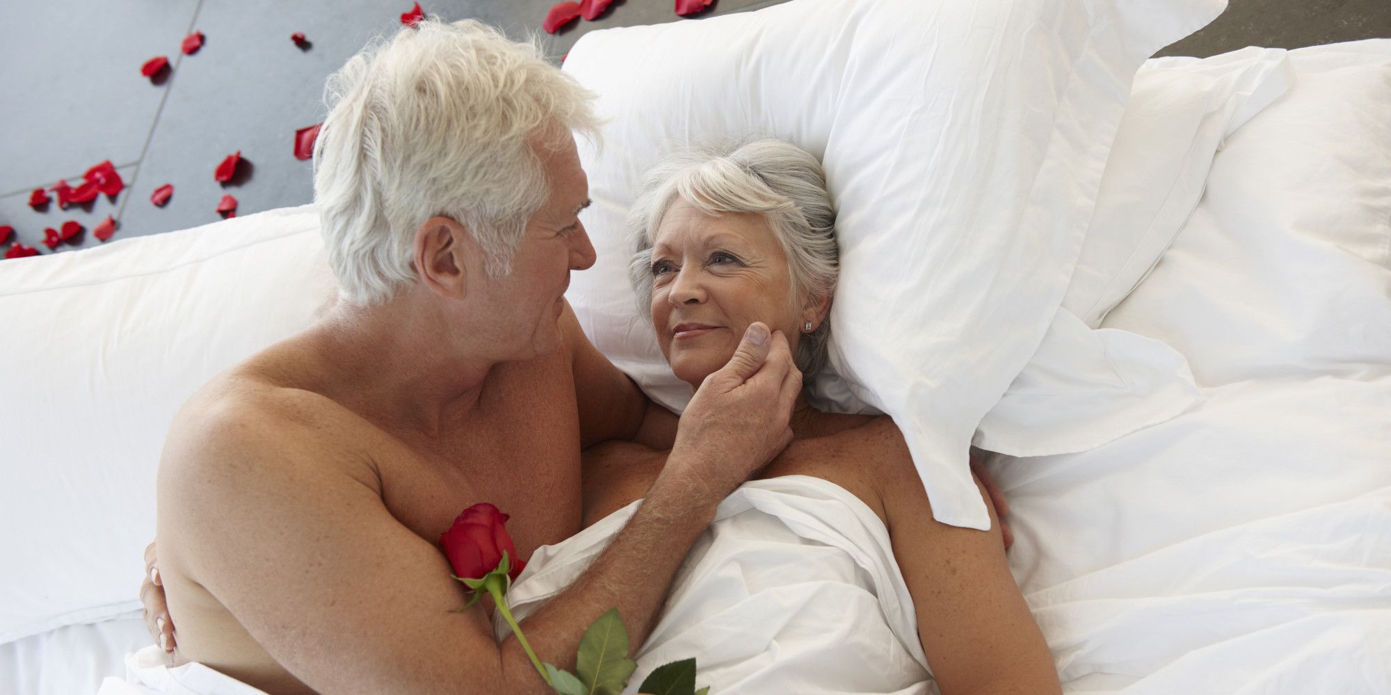 A photo of a older couple in bed together surround by red roses
